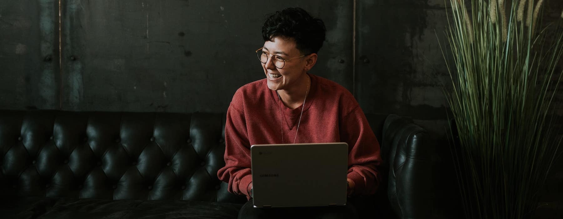 a woman smiling in a warm-toned room with a laptop on her lap